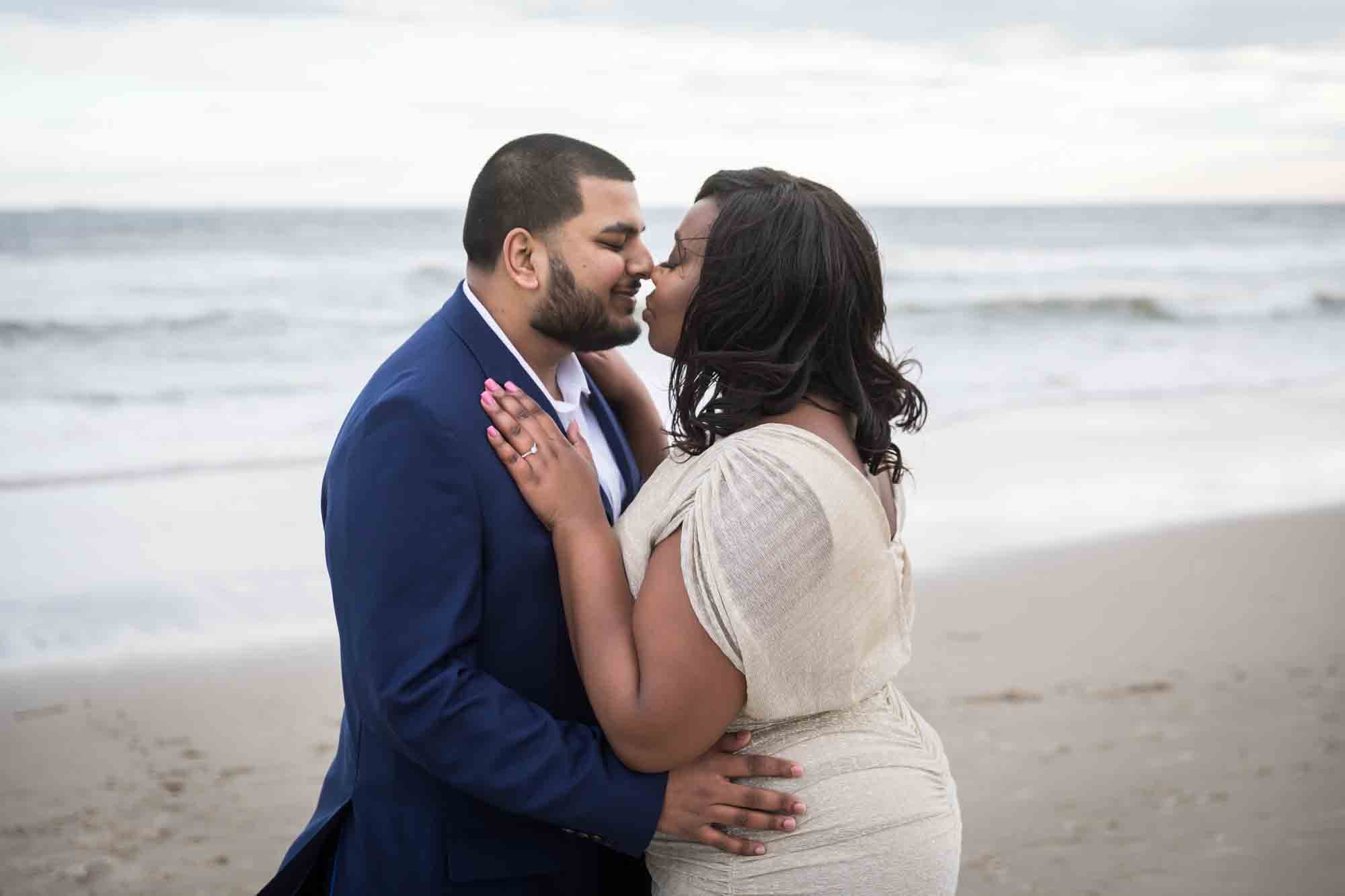 Couple kissing in front of waves for an article on how to plan the perfect beach engagement photo shoot