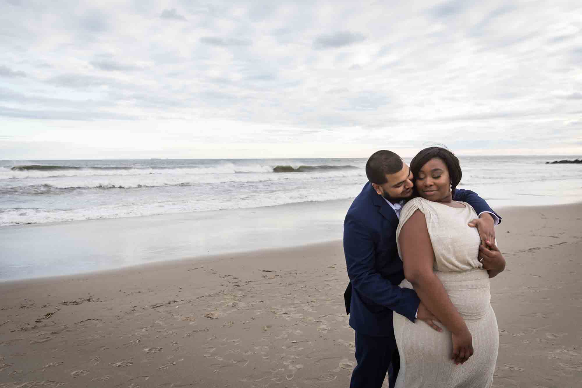 Couple hugging in front of waves for an article on how to plan the perfect beach engagement photo shoot