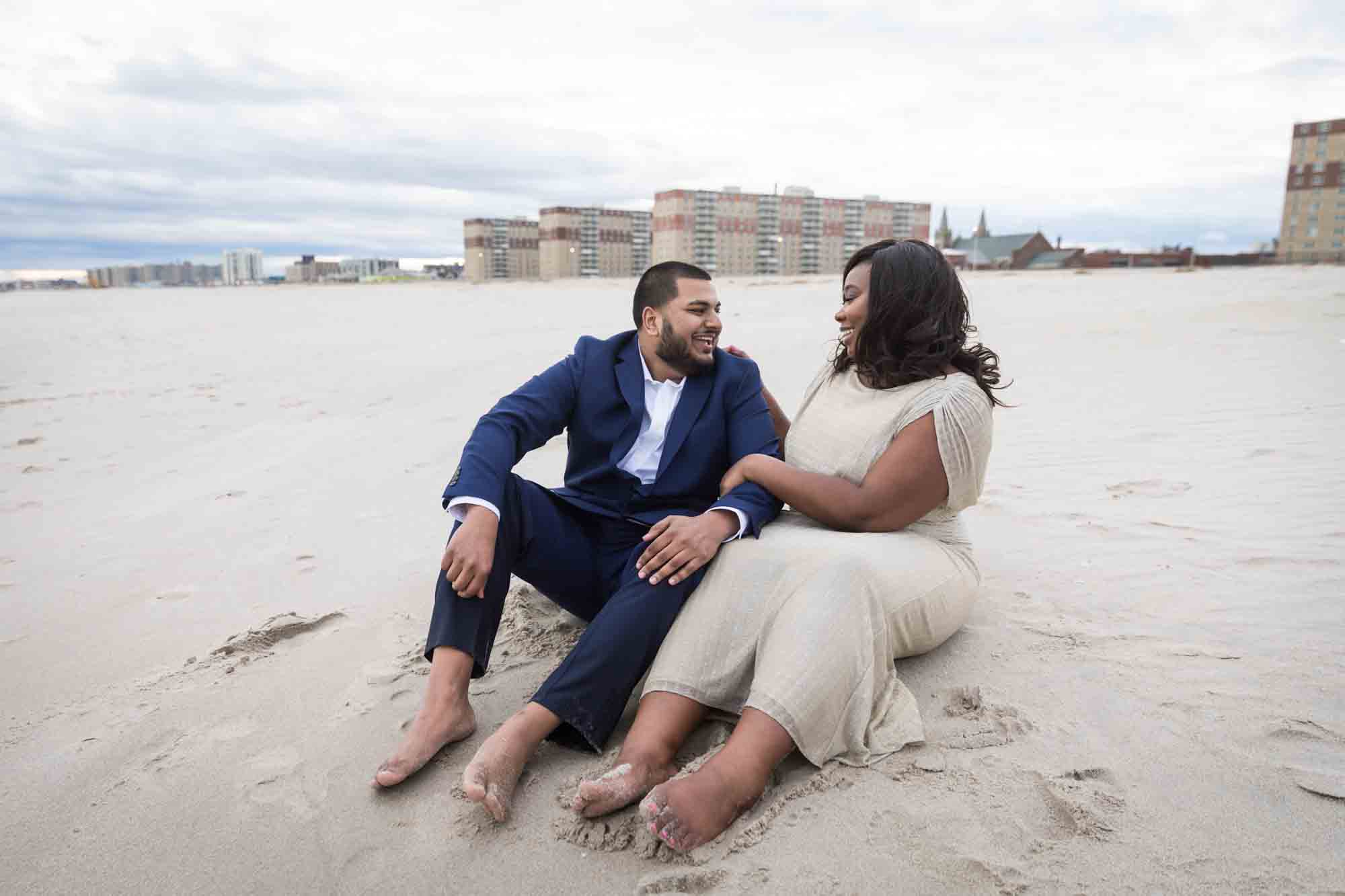 Couple sitting in the sand for an article on how to plan the perfect beach engagement photo shoot