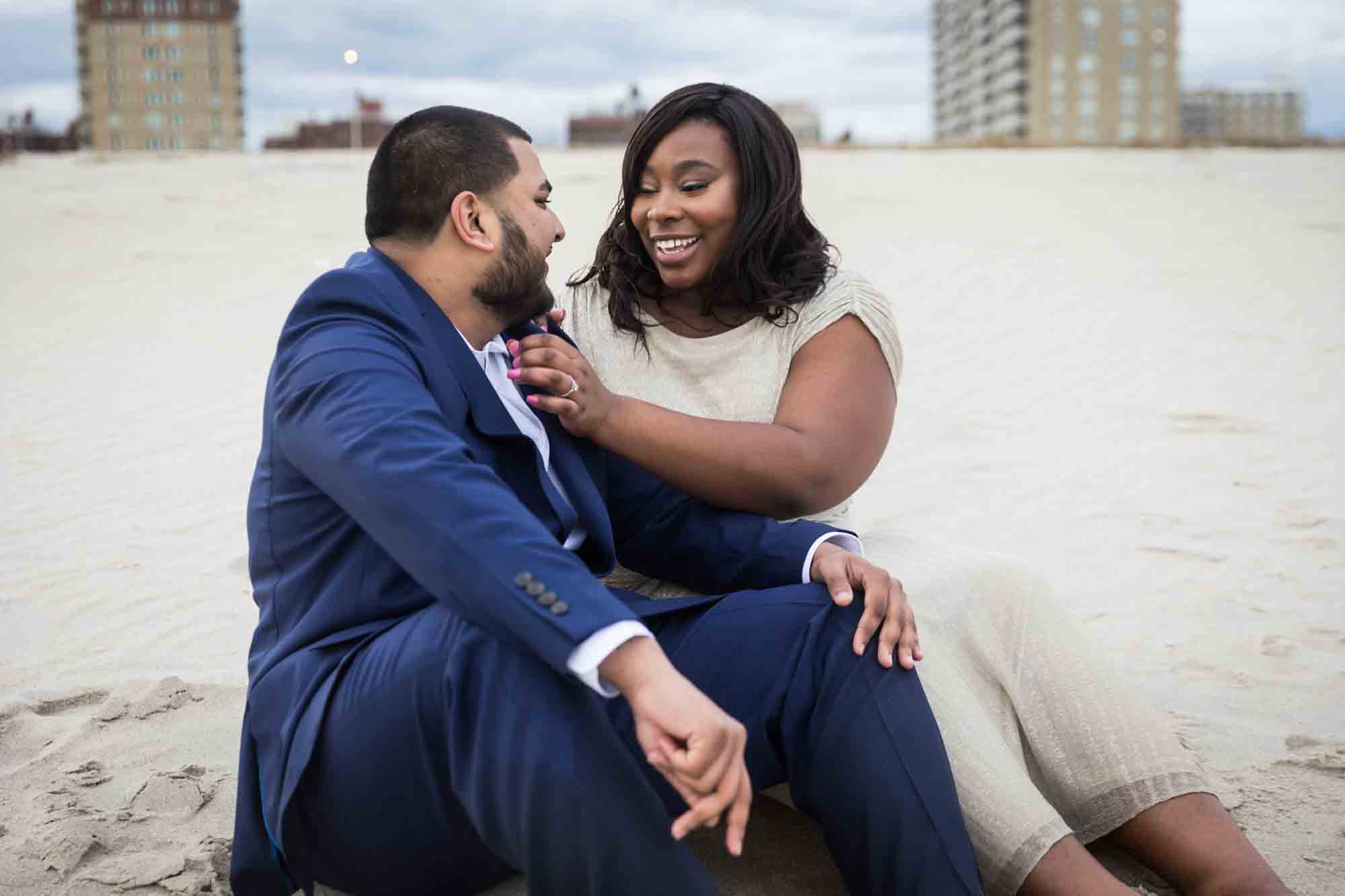 Couple sitting in the sand and laughing for an article on how to plan the perfect beach engagement photo shoot