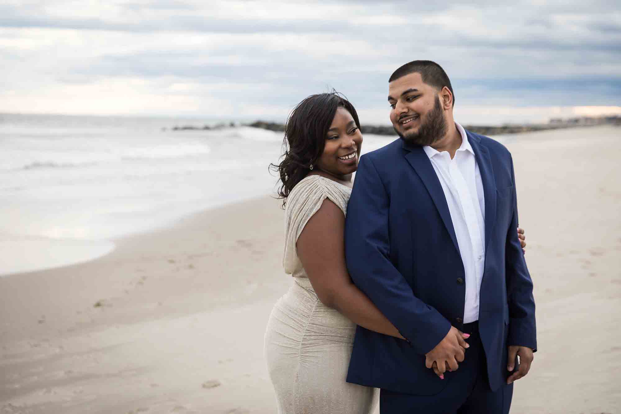 Couple cuddling on the beach for an article on how to plan the perfect beach engagement photo shoot