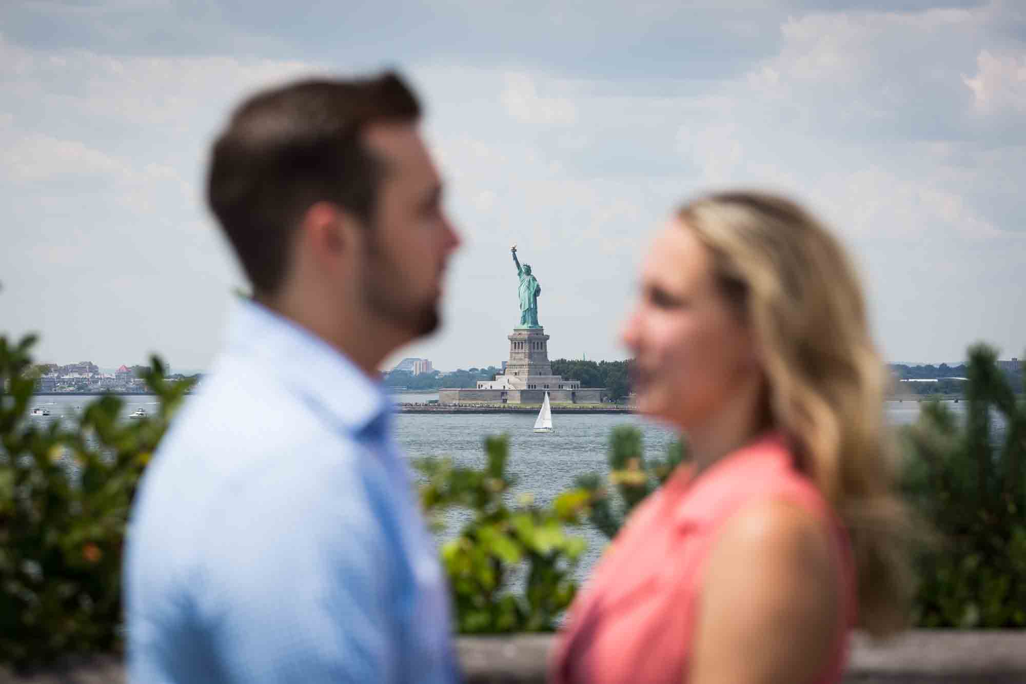 Statue of Liberty in background with couple out of focus in the foreground