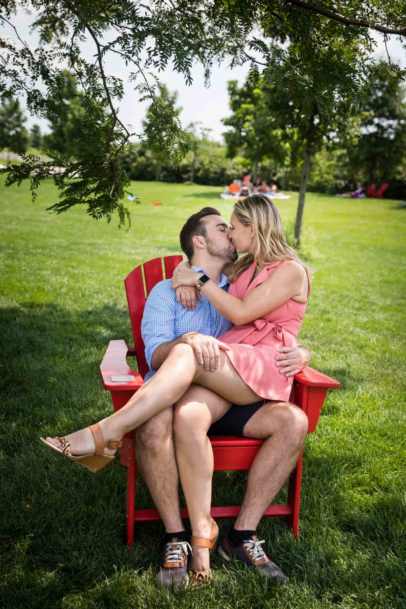 Couple kissing while seated on red Adirondack chair