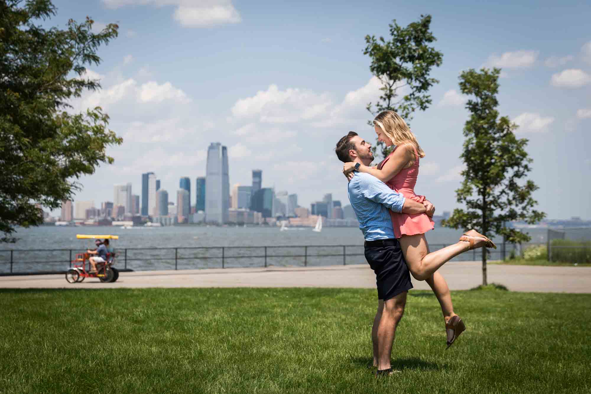 Man lifting woman up in the air with NYC skyline in the background