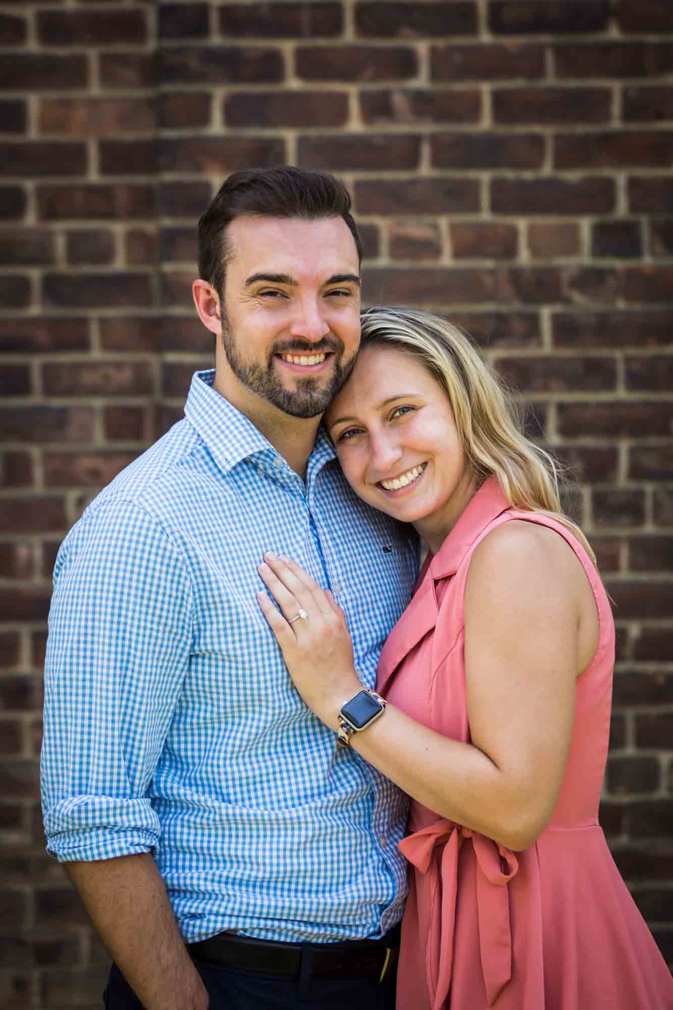 Couple in front of brick wall for an article on how to propose on Governors Island