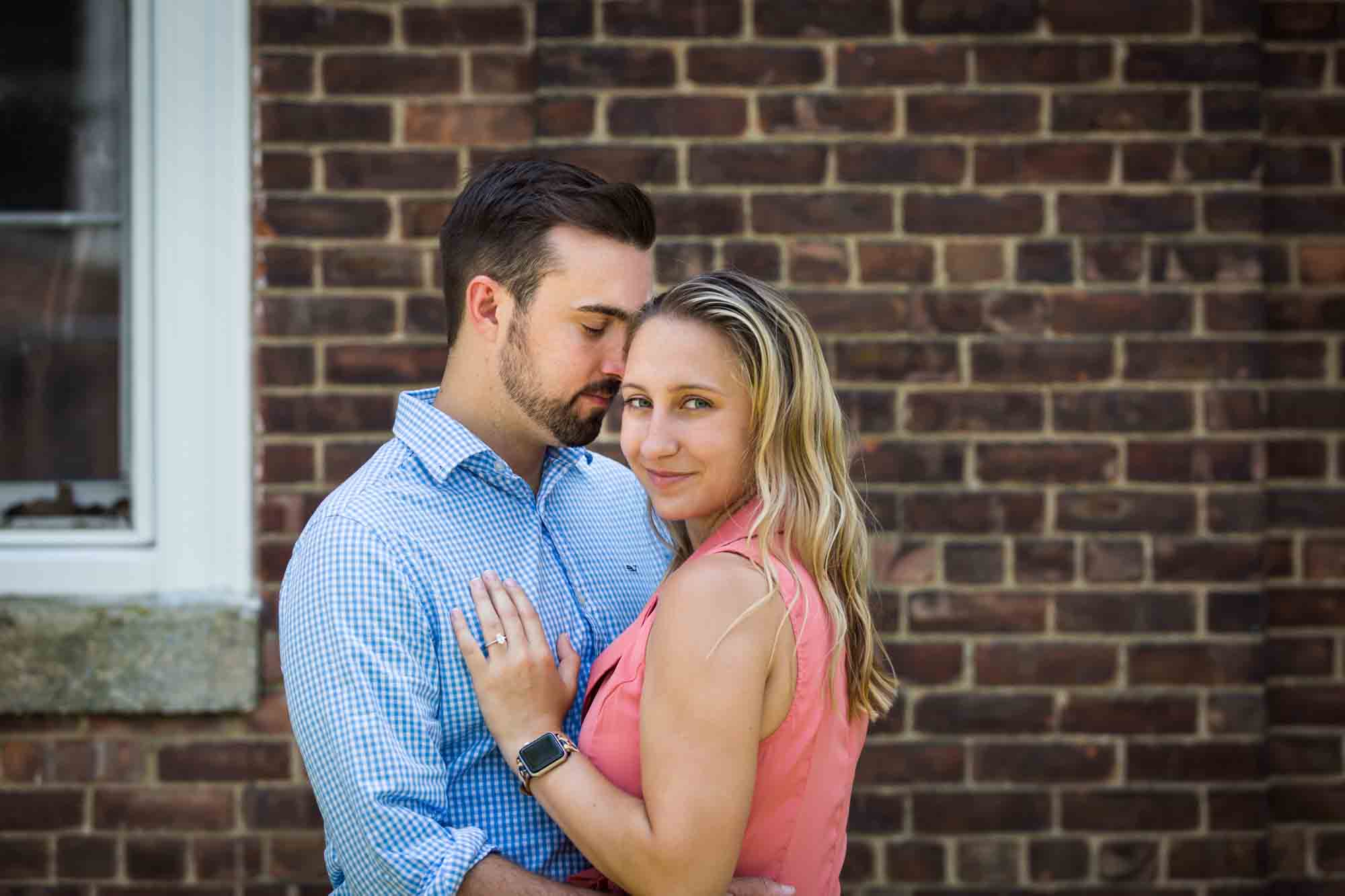 Couple hugging in front of brick wall for an article on how to propose on Governors Island