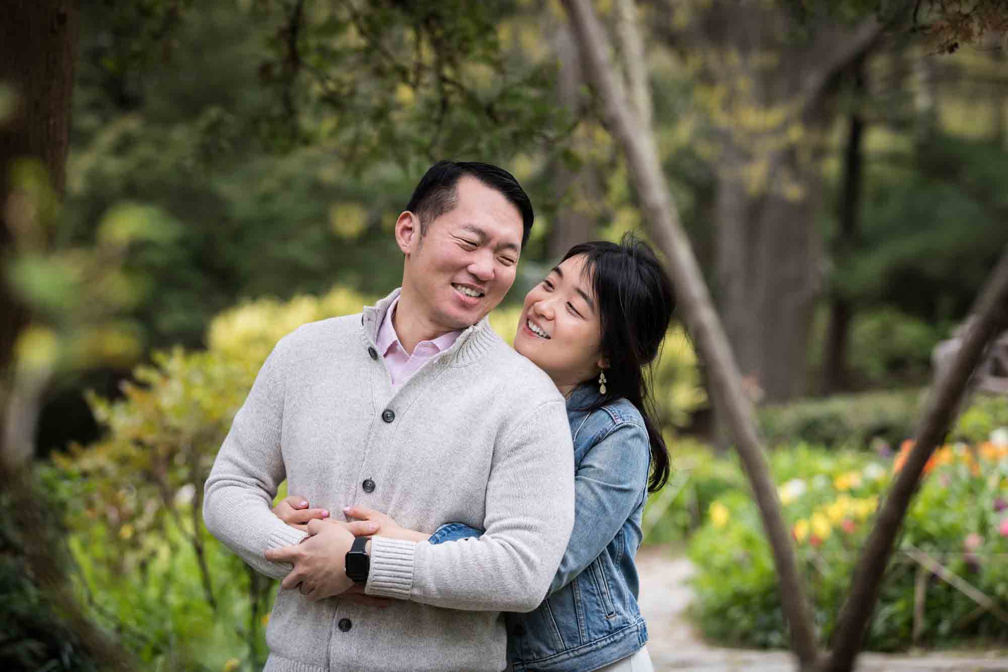Woman hugging man from behind in Shakespeare Garden during engagement shoot