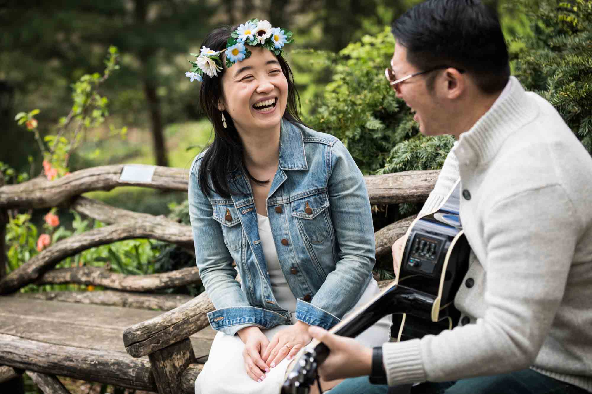 Shakespeare Garden engagement photos of man playing guitar for woman wearing daisies in her hair