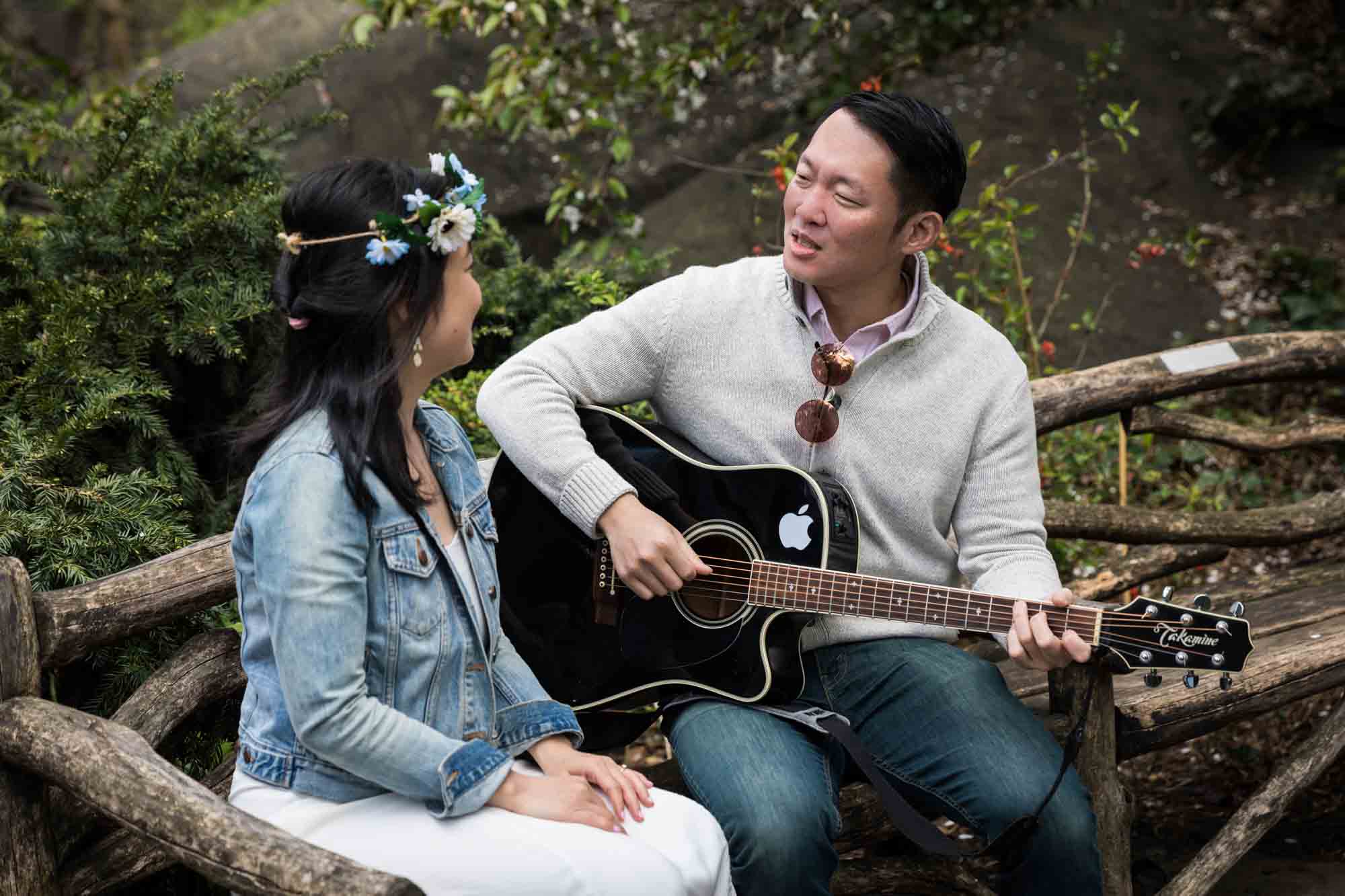 Man playing guitar for woman in Shakespeare Garden during engagement shoot
