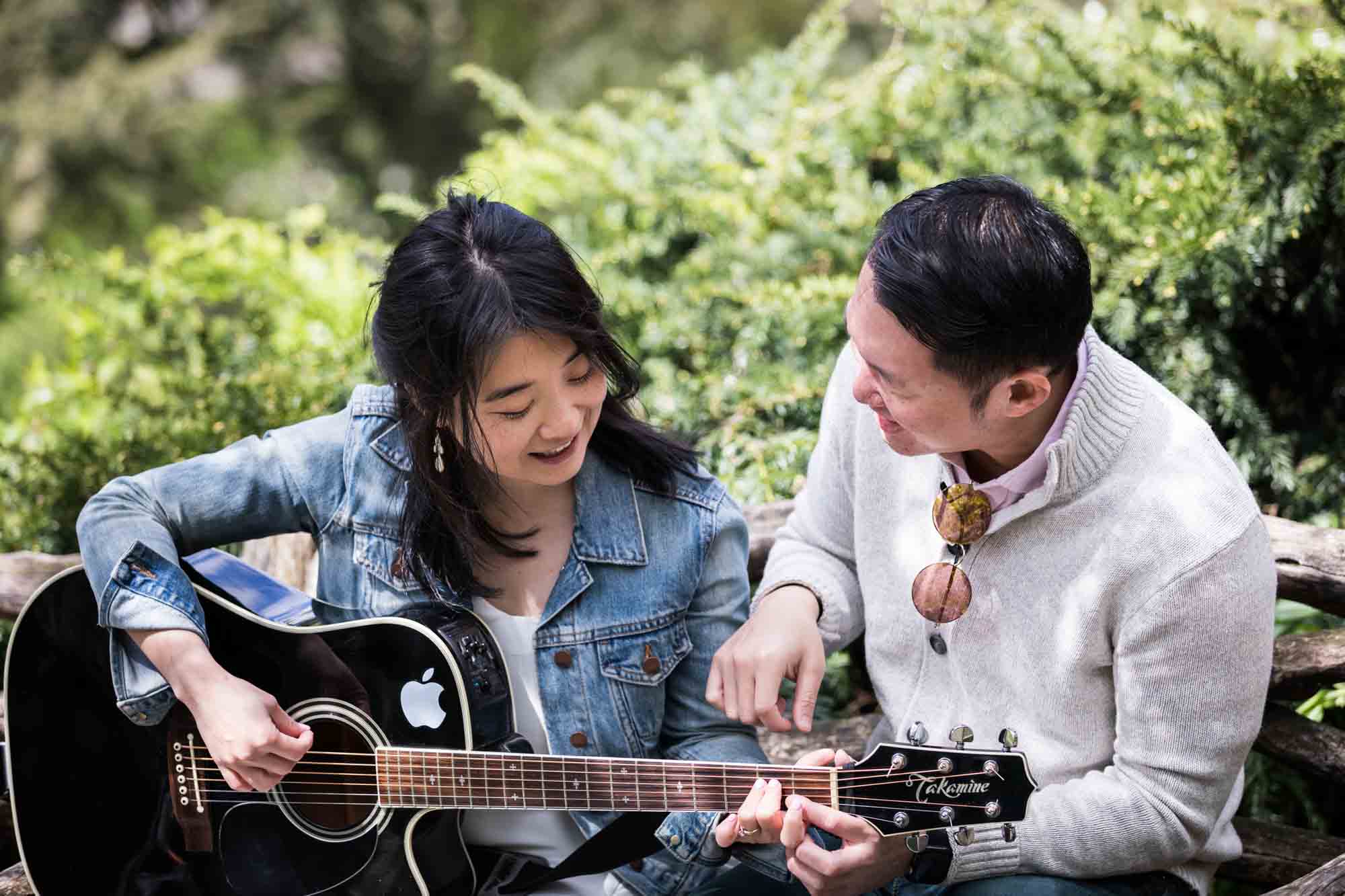 Man showing woman how to play guitar in Shakespeare Garden during engagement shoot