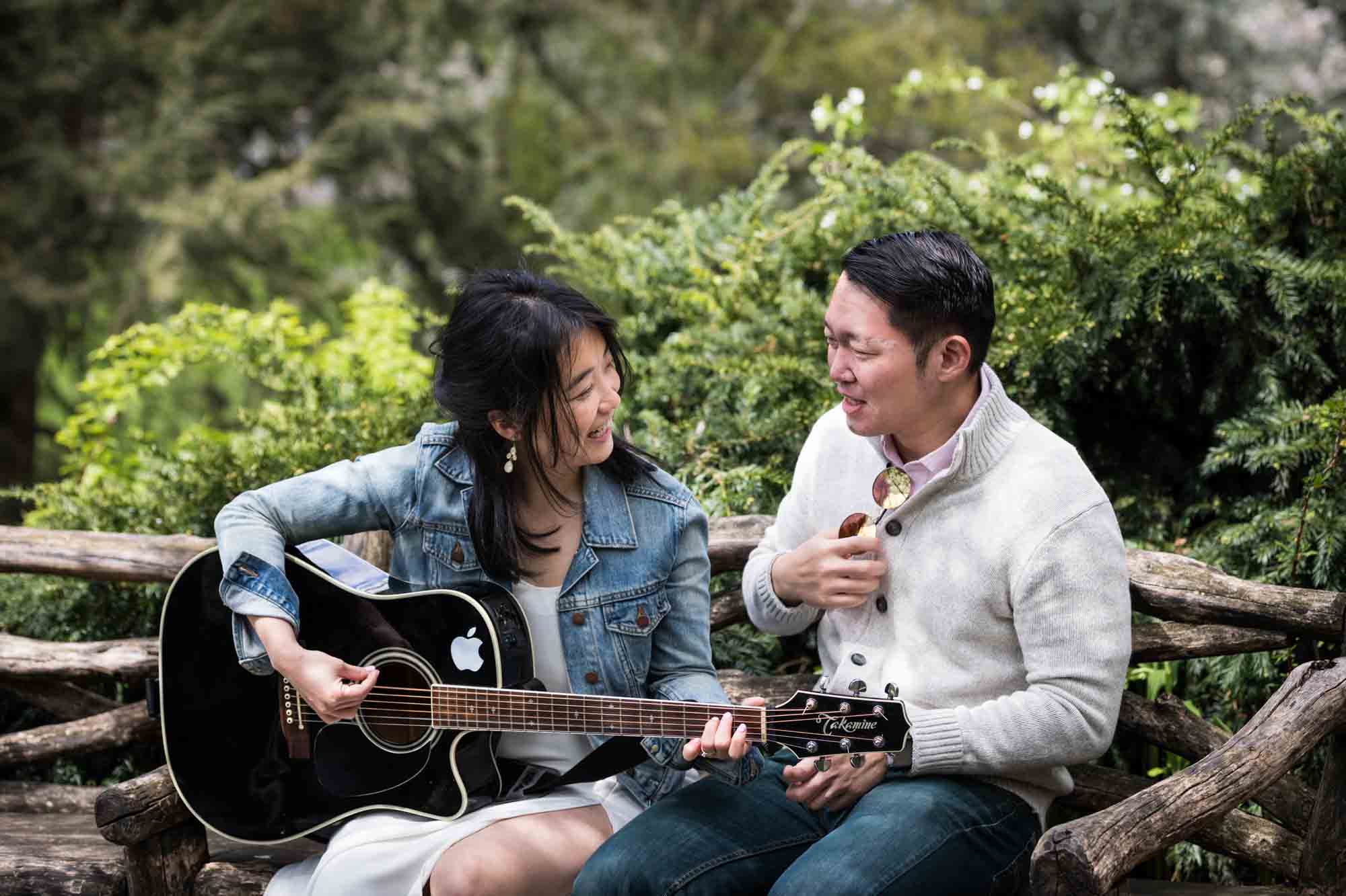 Man showing woman how to play guitar in Shakespeare Garden during engagement shoot