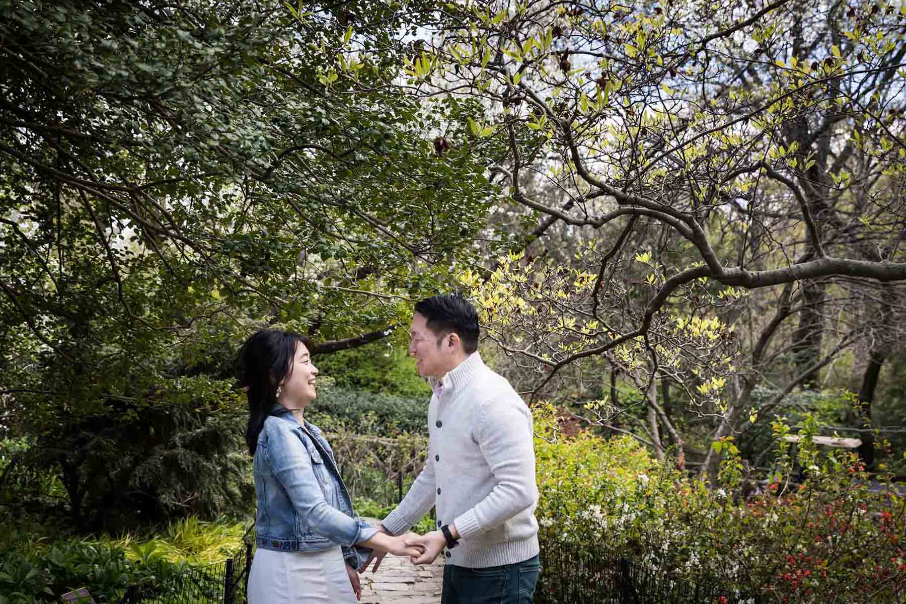 Couple holding hands under trees in Shakespeare Garden during engagement shoot