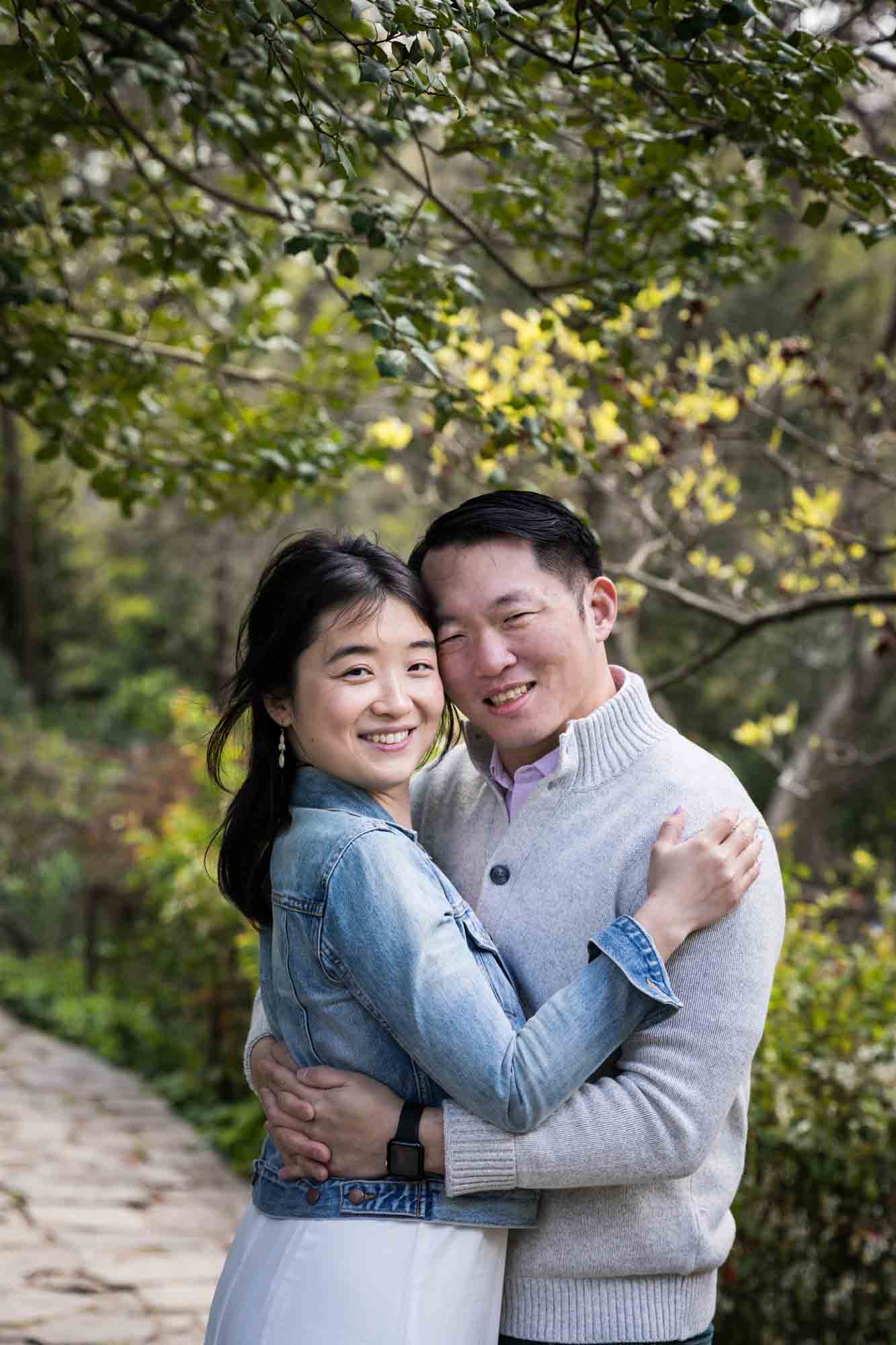 Couple hugging under trees in Shakespeare Garden during engagement shoot