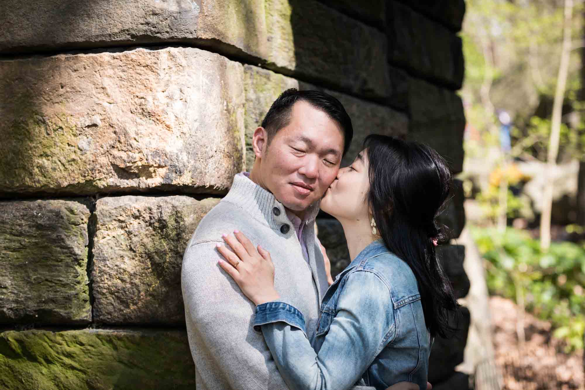 Woman kissing man's cheek in front of the Stone Arch in Central Park