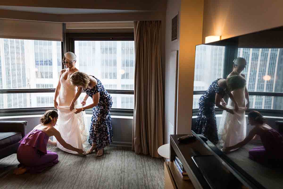 Women assisting bride get into dress reflected in TV