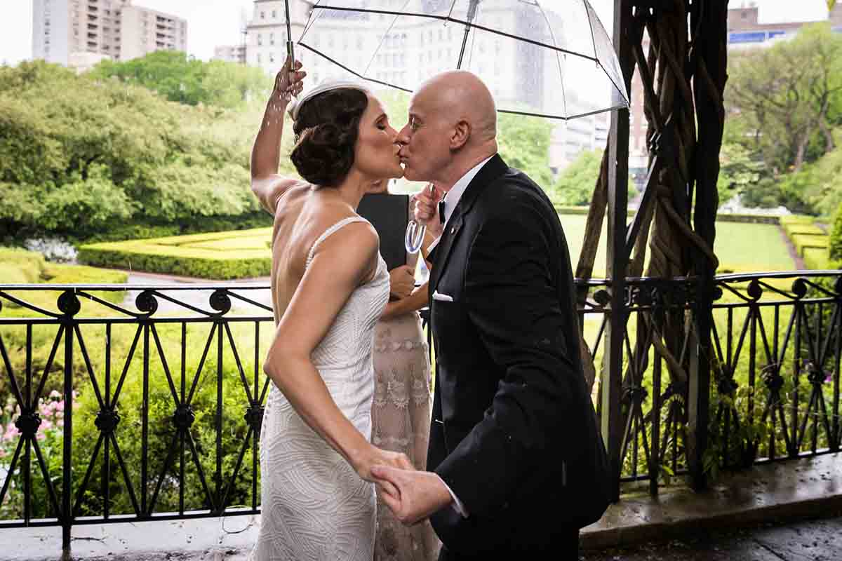 Central Park Wisteria Pergola wedding photos of bride and groom kissing while holding umbrellas