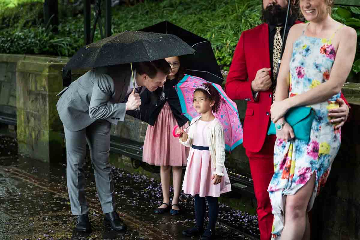 Central Park Wisteria Pergola wedding photos of father speaking to little girl wearing a tiara and holding a pink umbrella