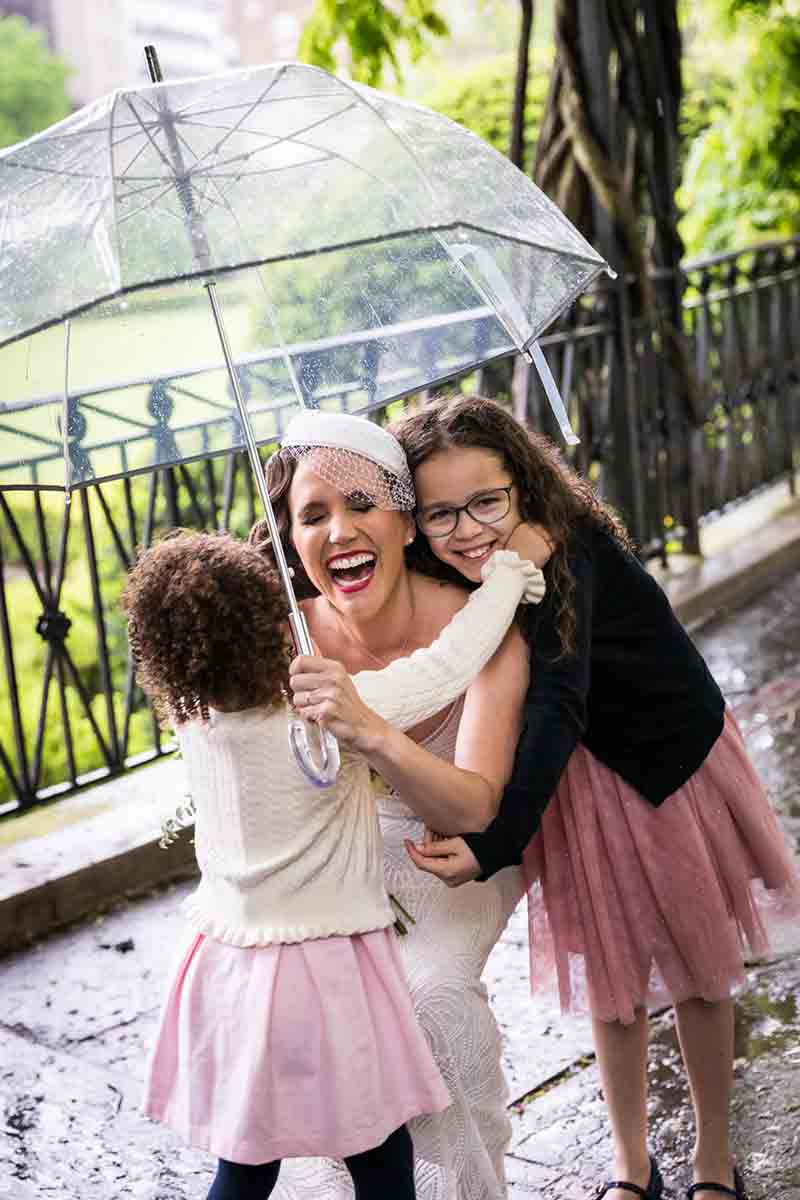 Central Park Wisteria Pergola wedding photos of bride hugging two little girls and holding clear umbrella