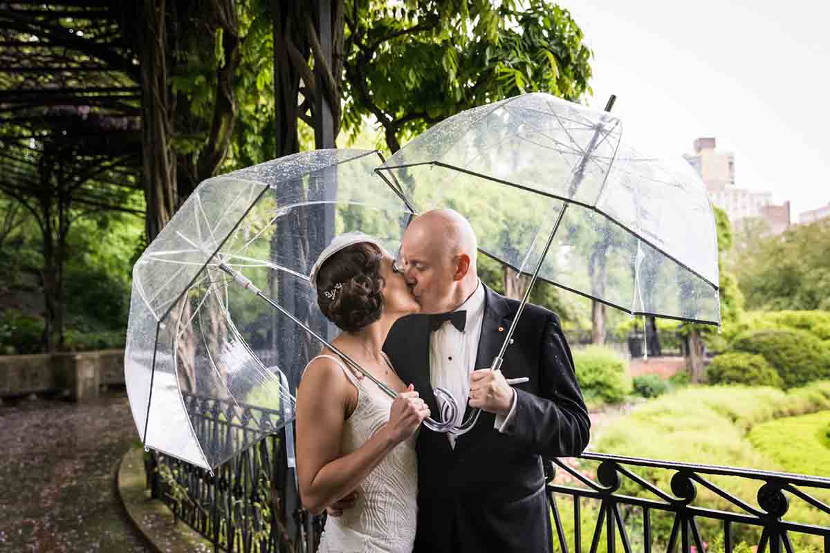 Central Park Wisteria Pergola wedding photos of bride and groom kissing and holding clear umbrellas