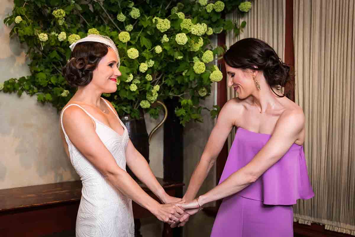 Bride holding hands with female guest wearing pink jumpsuit