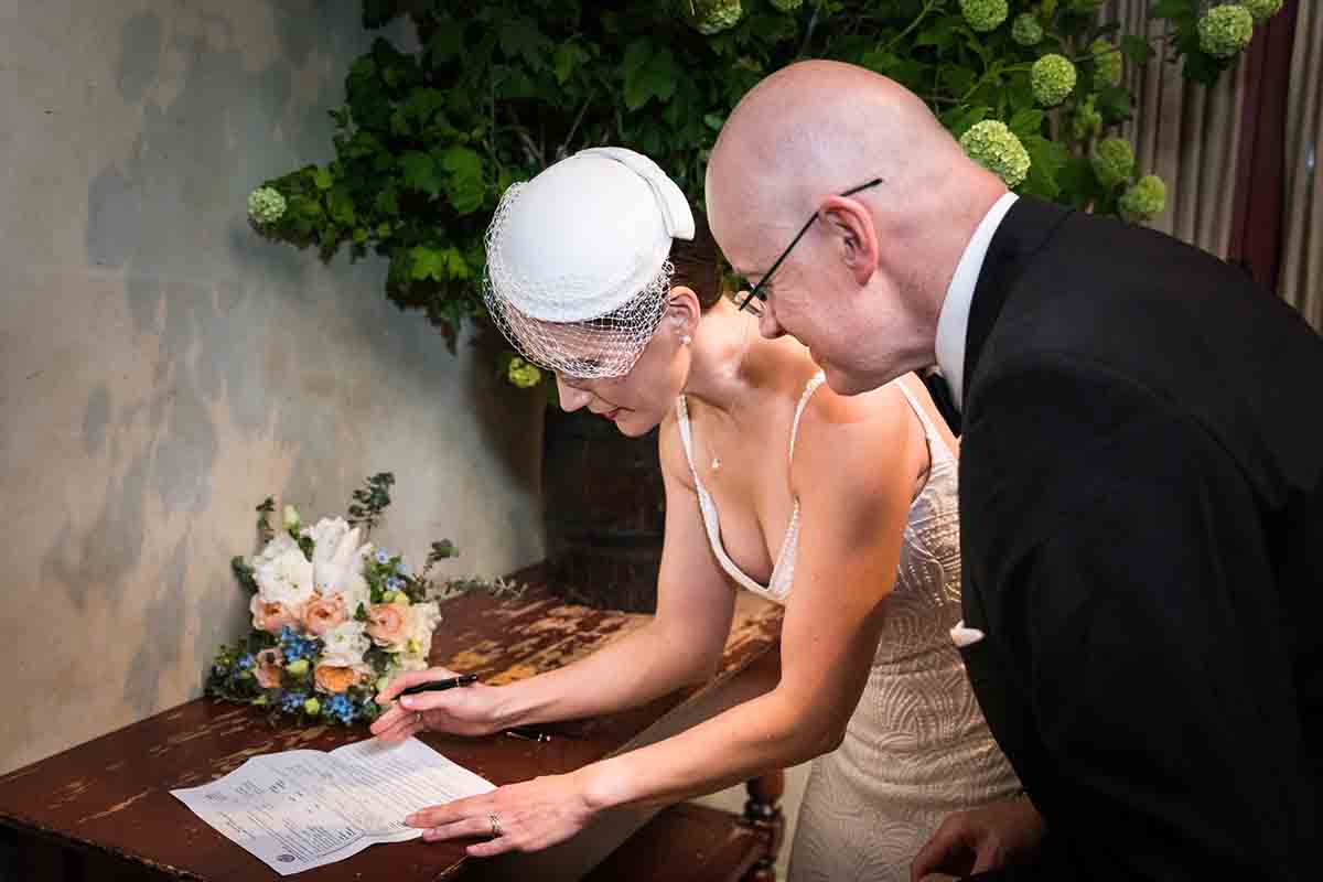 Bride and groom signing marriage certificate on table