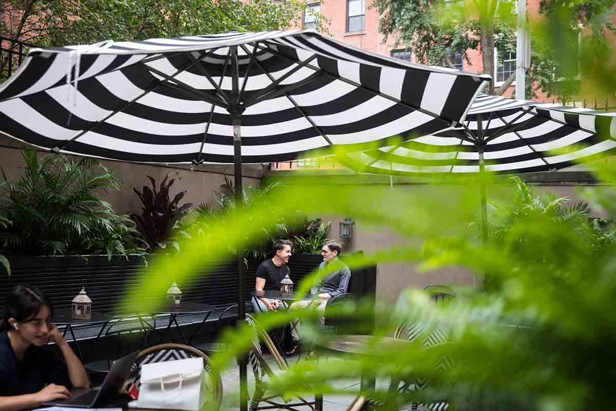 Two men at an outdoor table underneath a black and white umbrella at the High Line Hotel
