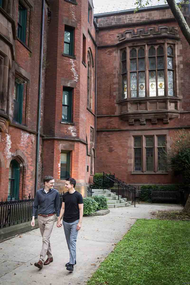 Two men holding hands and walking along pathway in front of brick facade of High Line Hotel