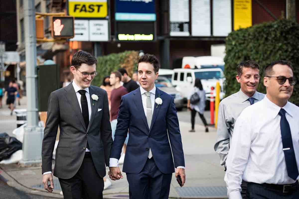 Two grooms holding hands and walking to NYC wedding reception
