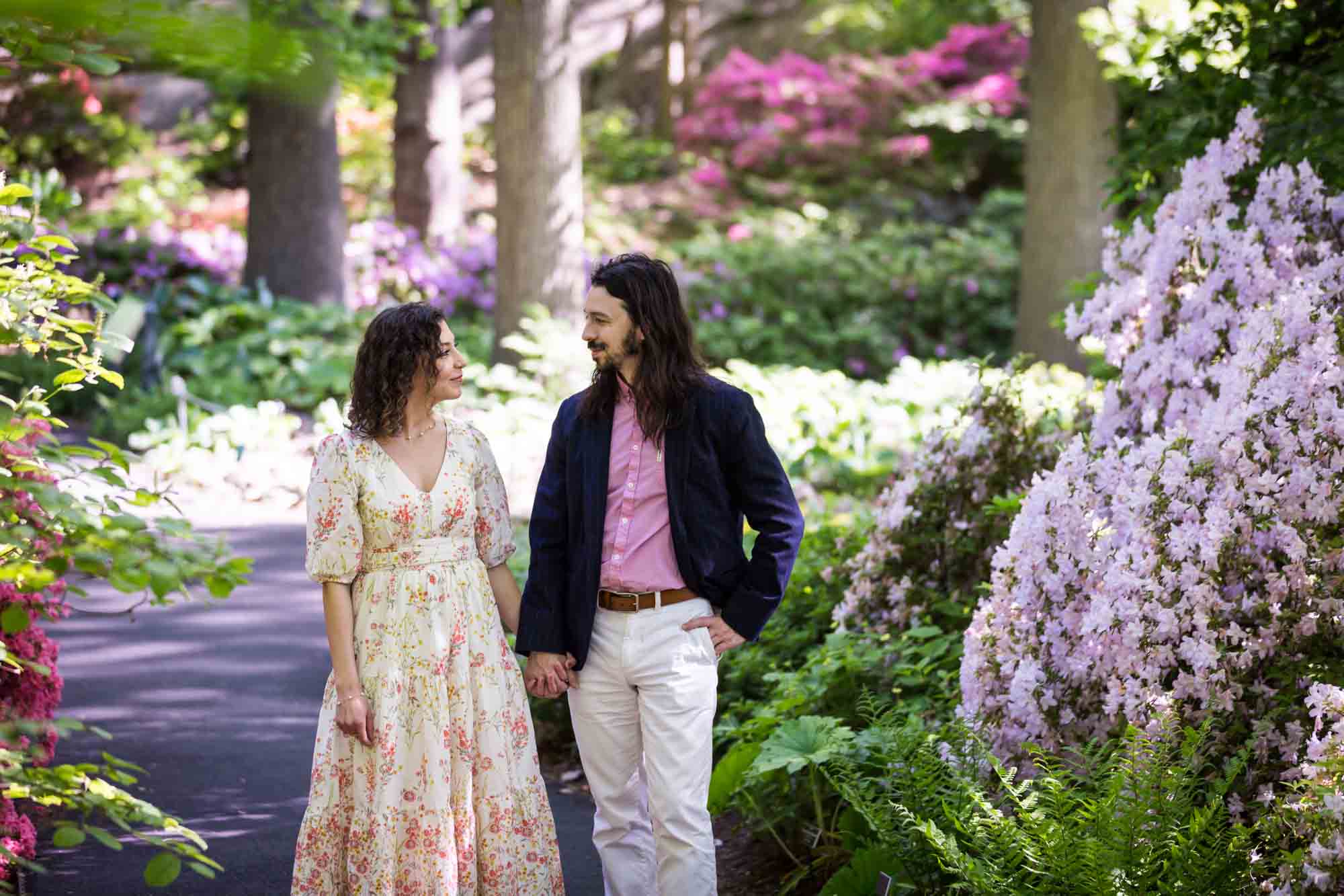 New York Botanical Garden engagement photos of couple walking down pathway surrounded by azaleas
