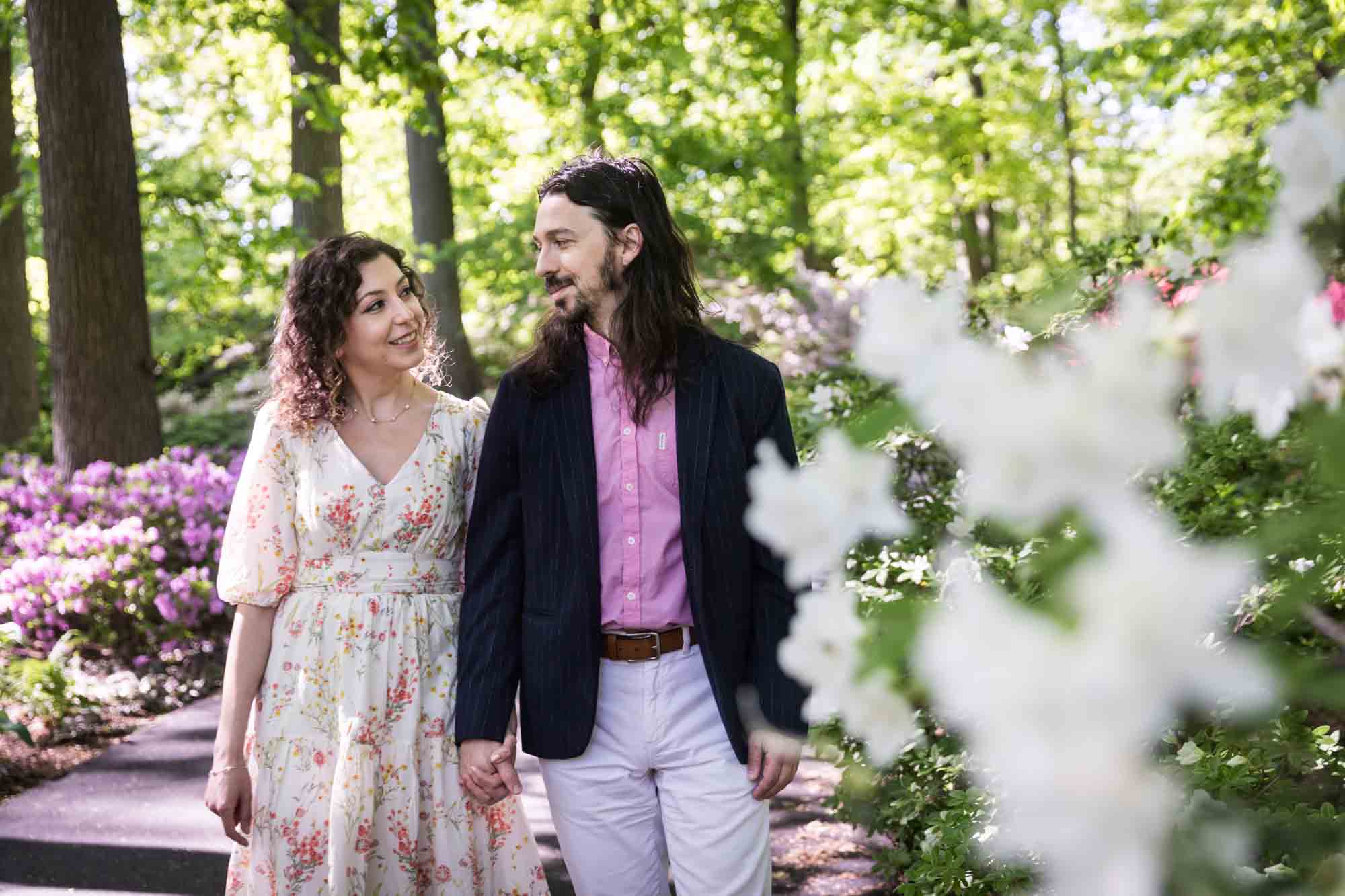 New York Botanical Garden engagement photos of couple walking down pathway surrounded by azaleas