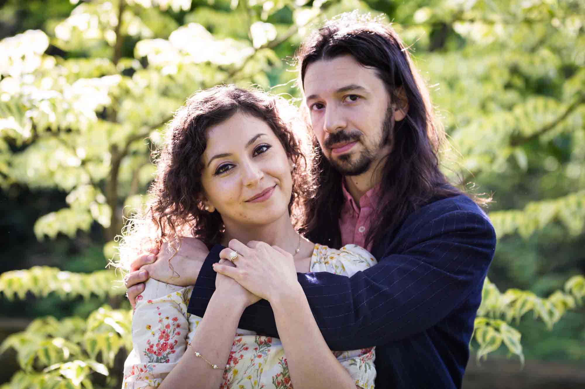 Man hugging woman's shoulders in New York Botanical Garden during engagement photo shoot