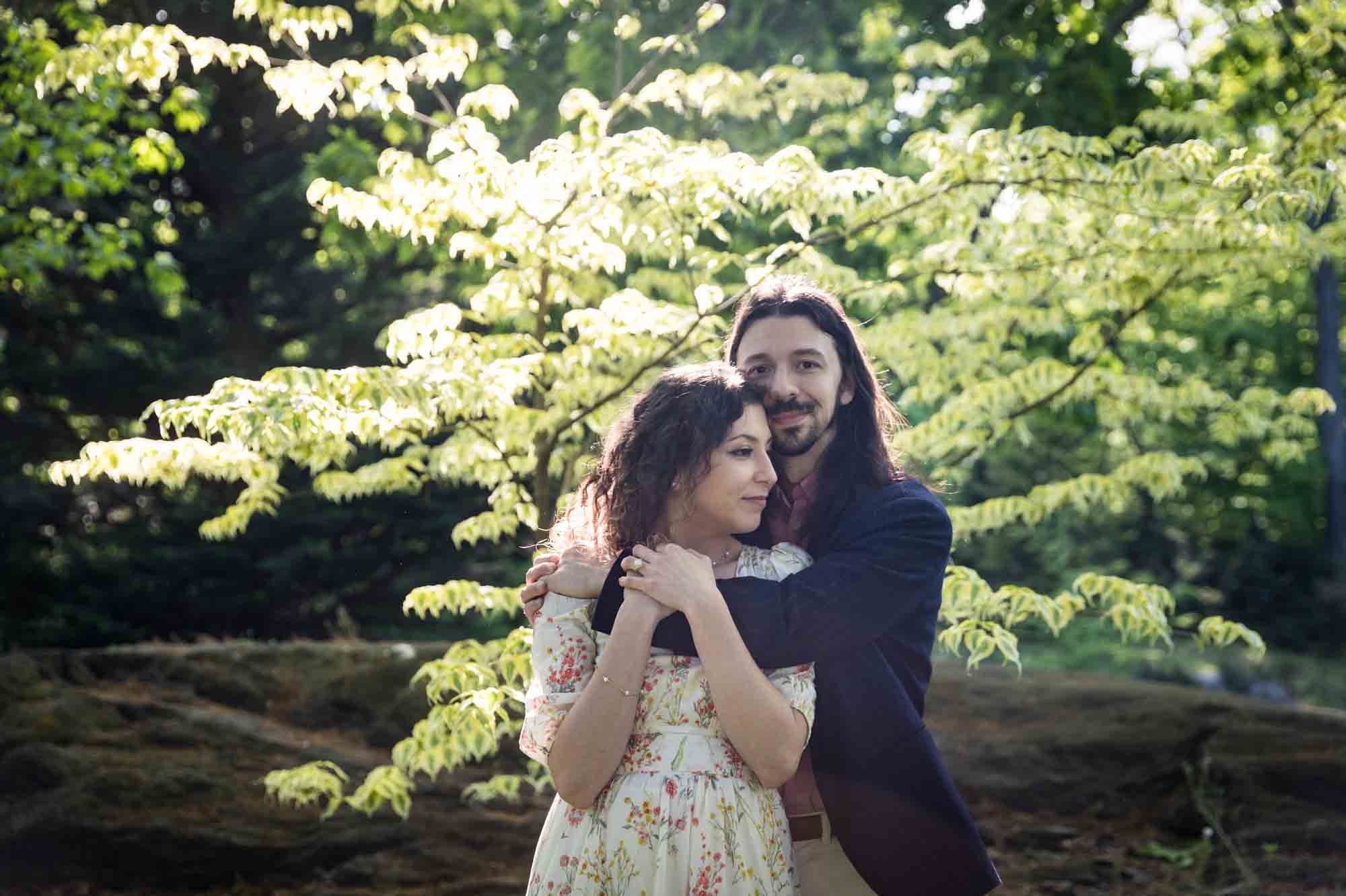 Man hugging woman by the shoulders in New York Botanical Garden during engagement photo shoot