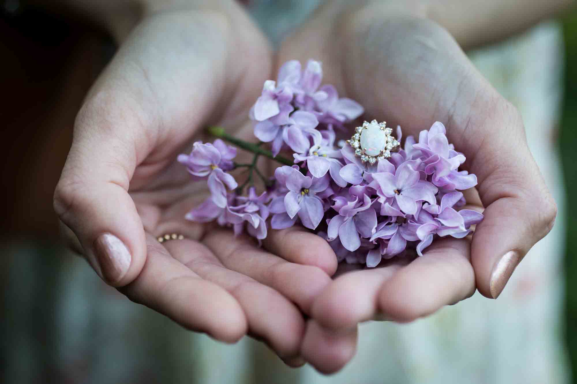 Woman's hands holding lilacs and opal engagement ring