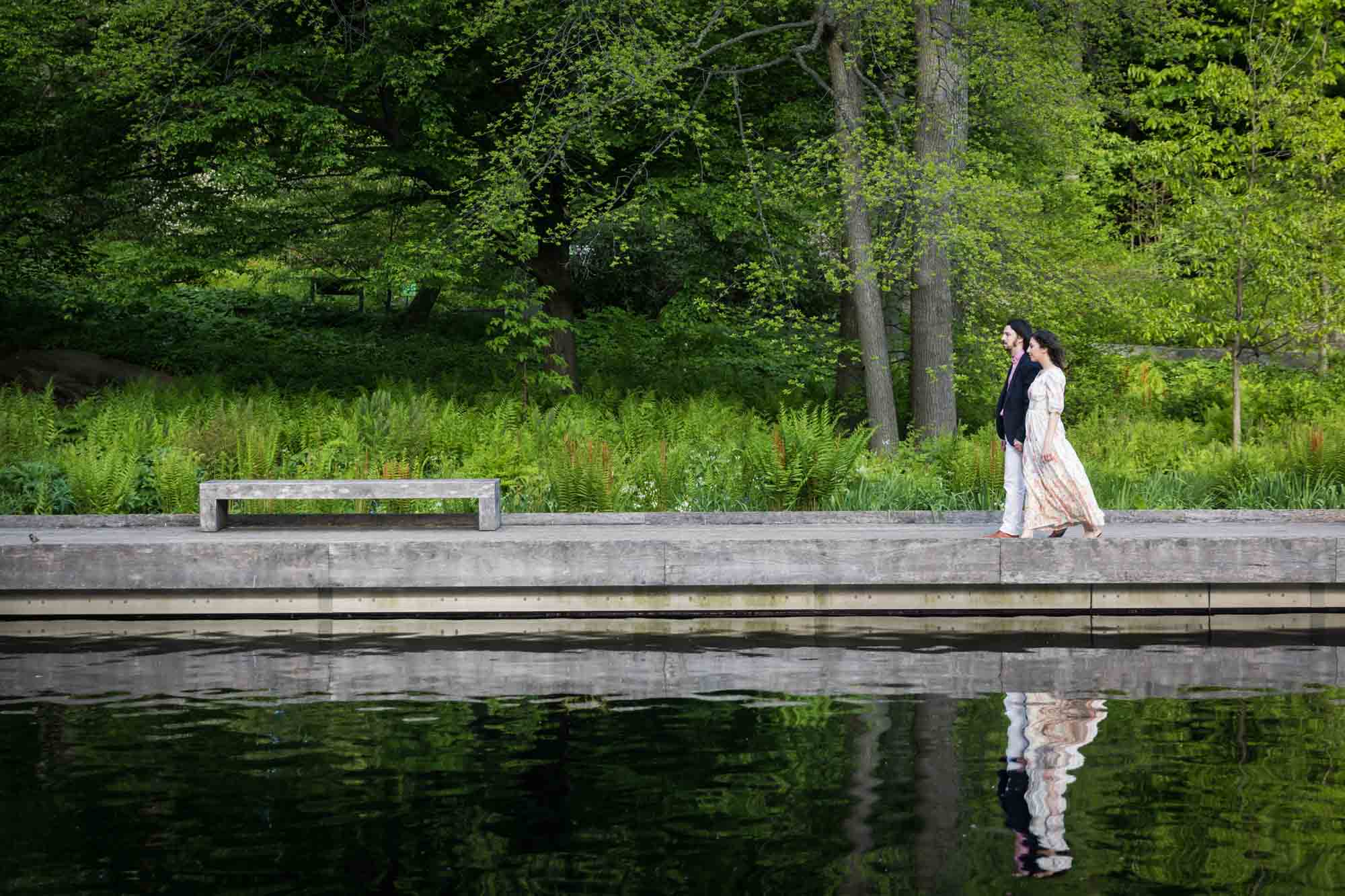 Couple walking beside pond and reflected in water in New York Botanical Garden