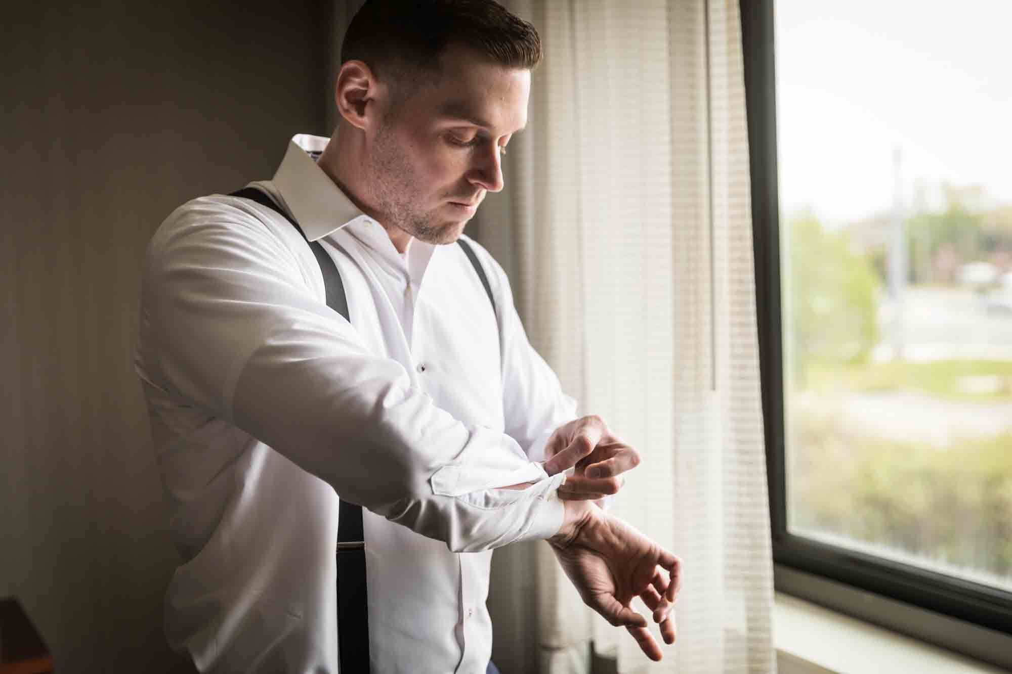 Groom putting on cufflinks in front of a window