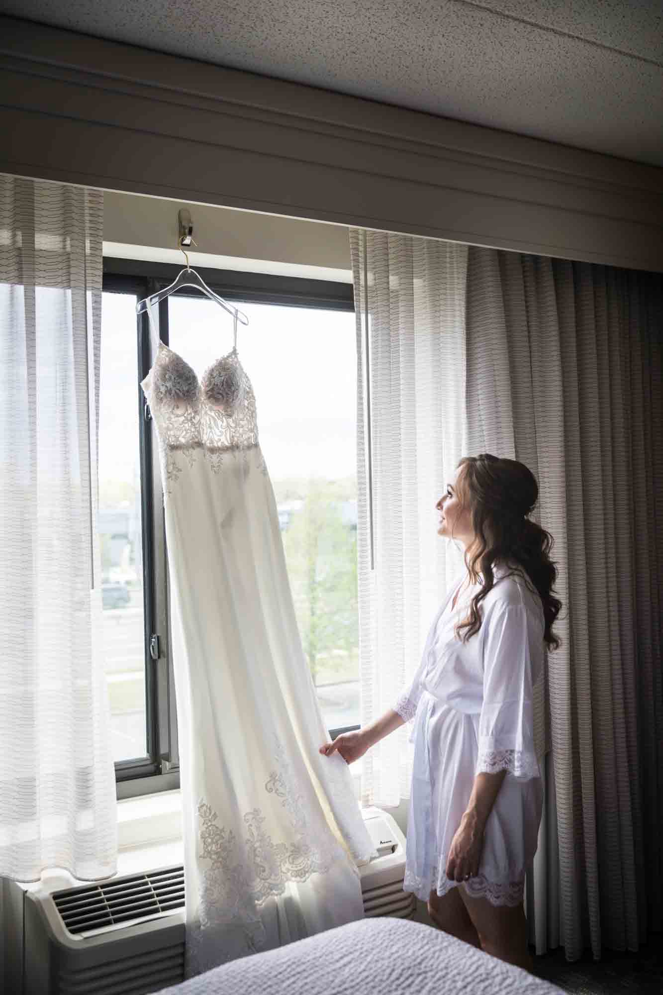 Bride looking up at wedding dress hanging on window