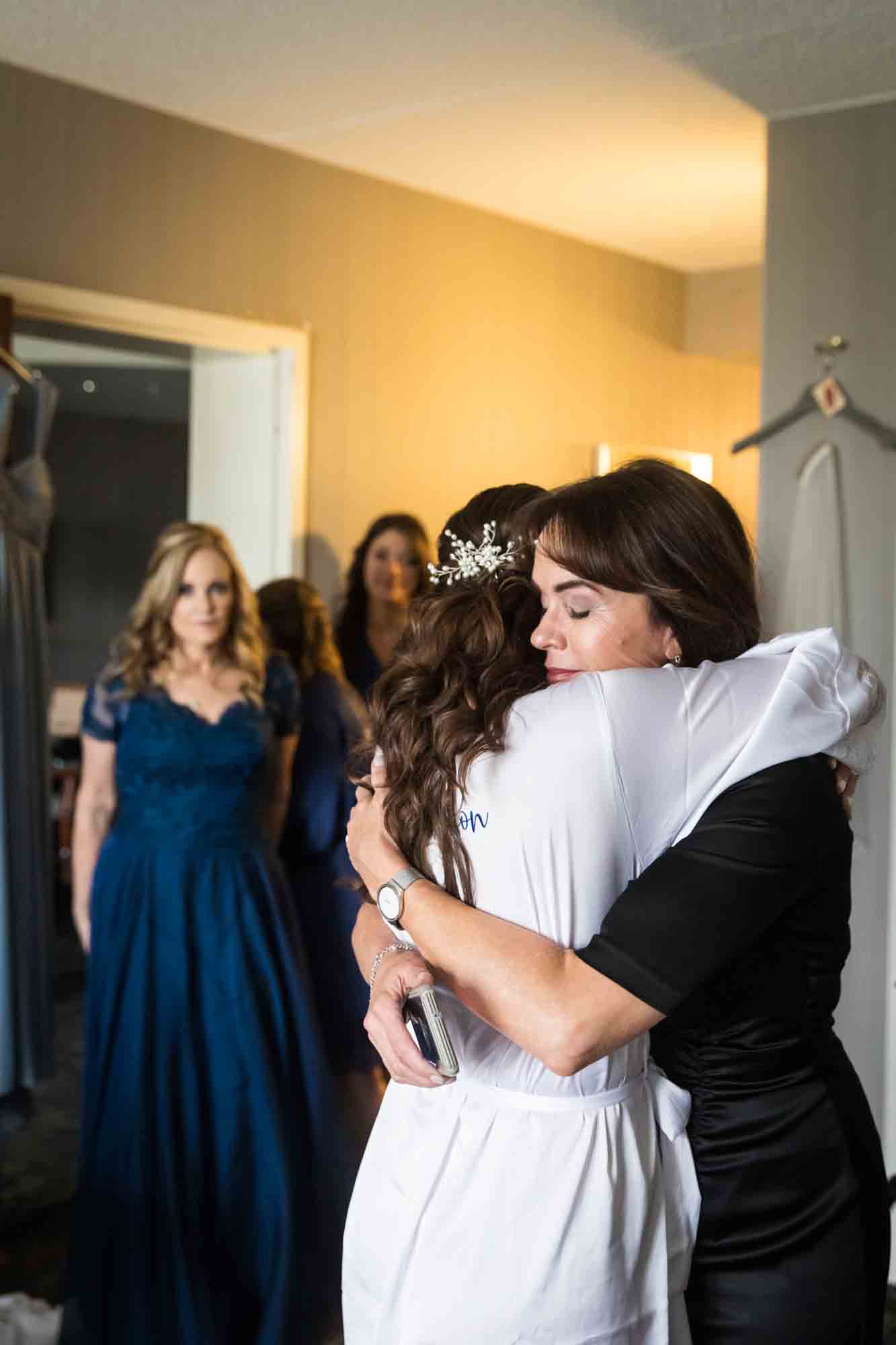 Woman hugging bride with other women in background watching