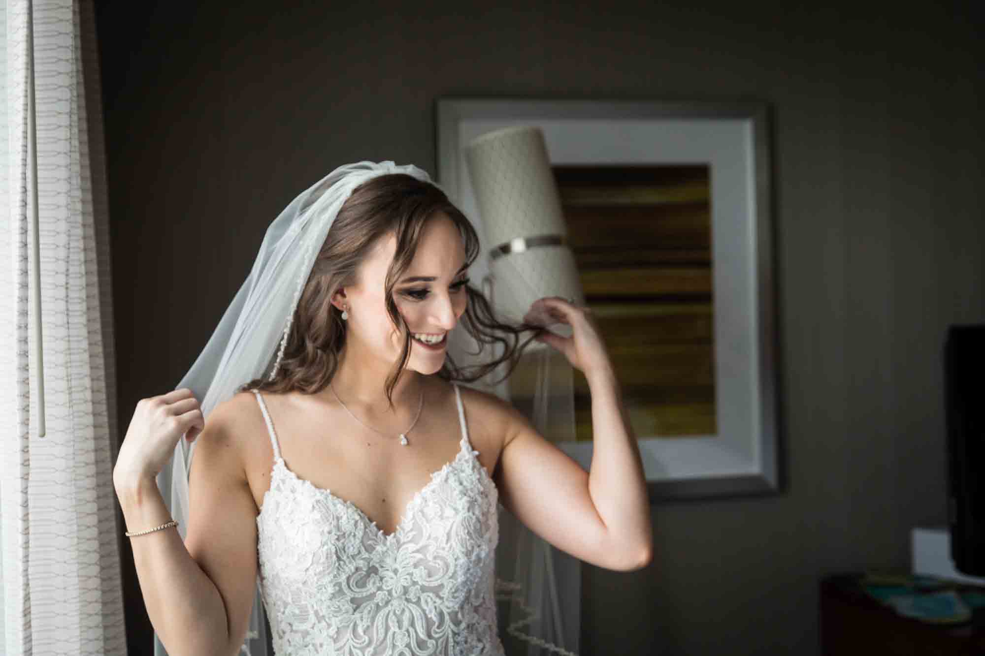 Bride in front of window adjusting her veil