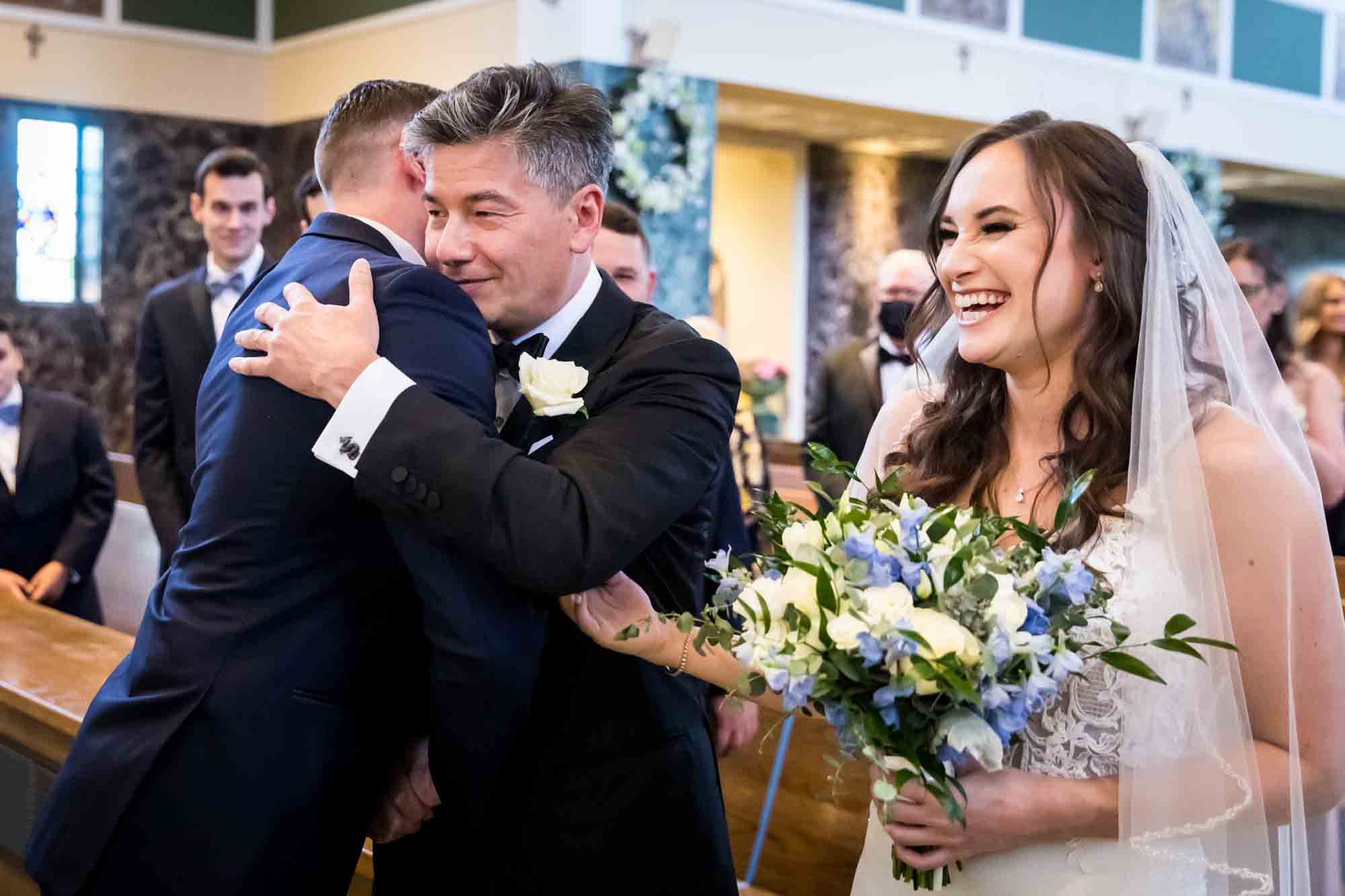 Father hugging groom with bride on side