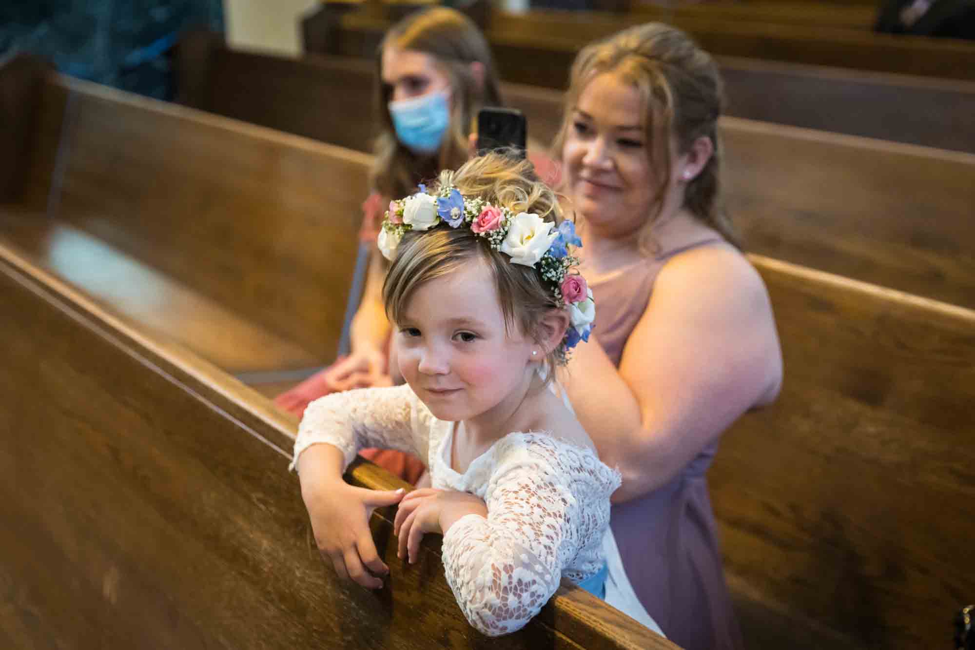 Little flower girl and female guests sitting in church pew