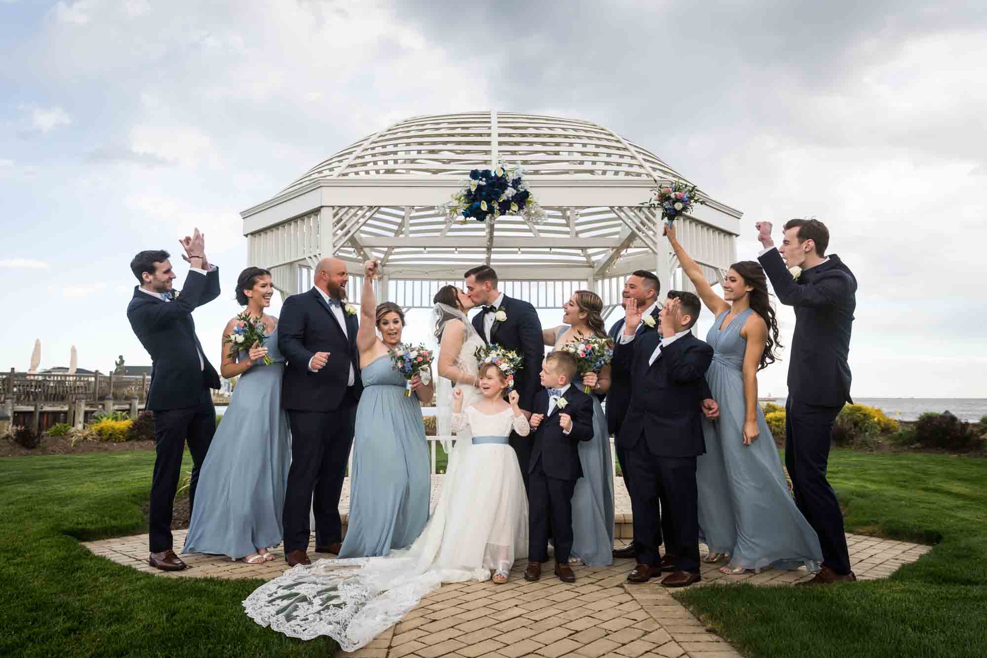 Bride and groom kissing in front of bridal party in front of white gazebo