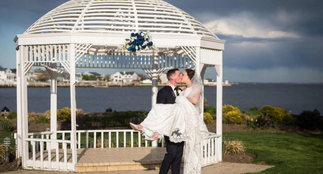 Riviera Waterfront Mansion wedding photos of groom carrying bride in front of white gazebo