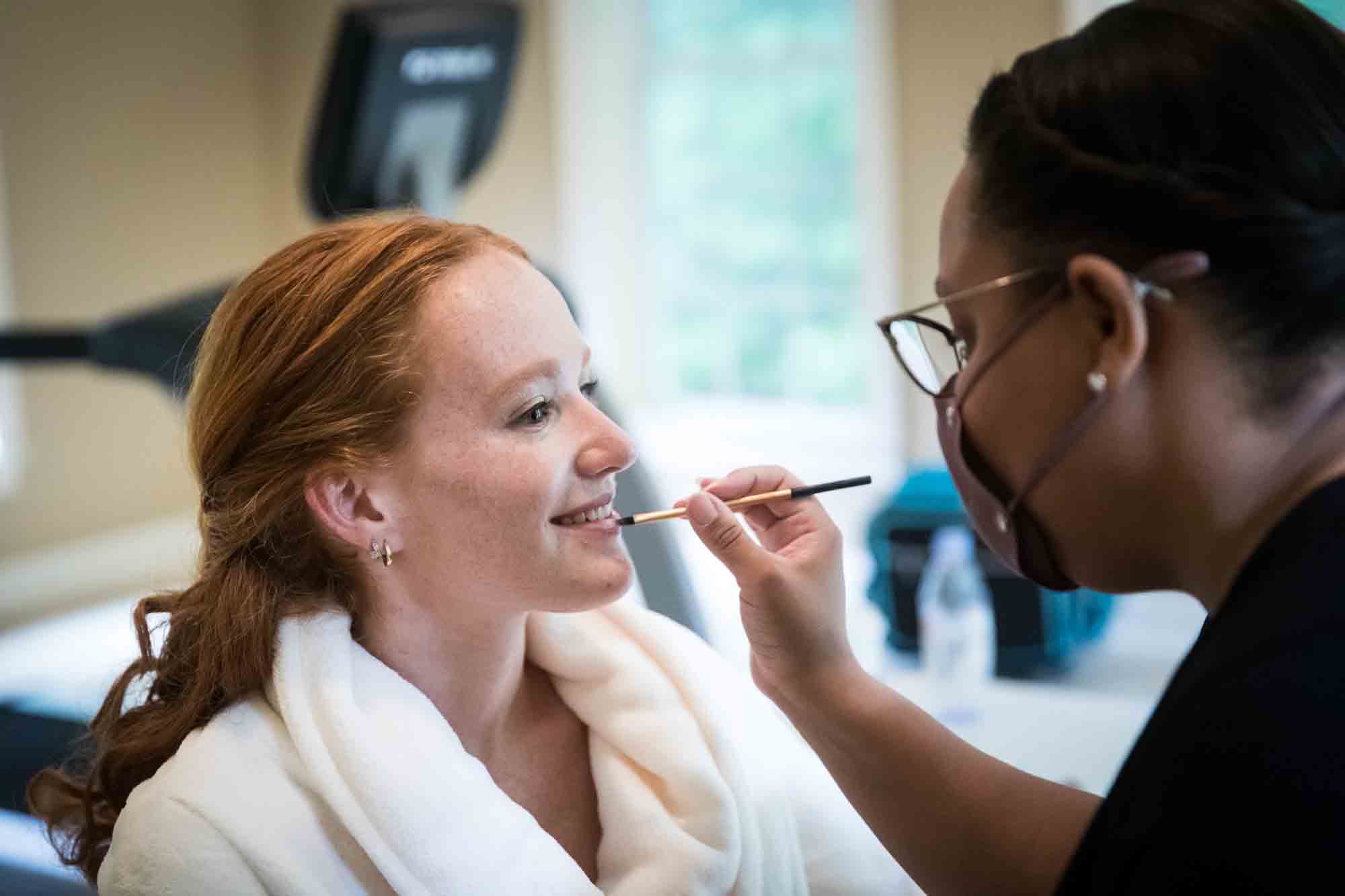 Woman with red hair wearing robe having lipstick applied