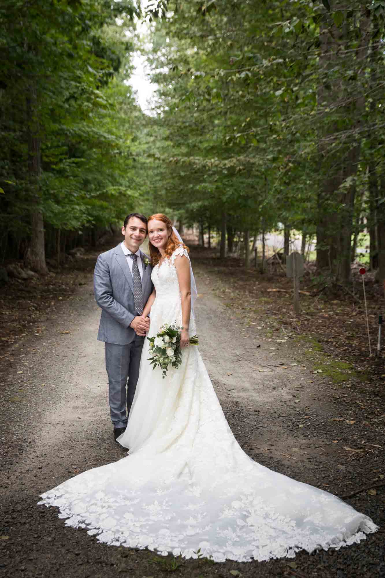 Bride with long train standing with groom in driveway for an article on backyard wedding tips