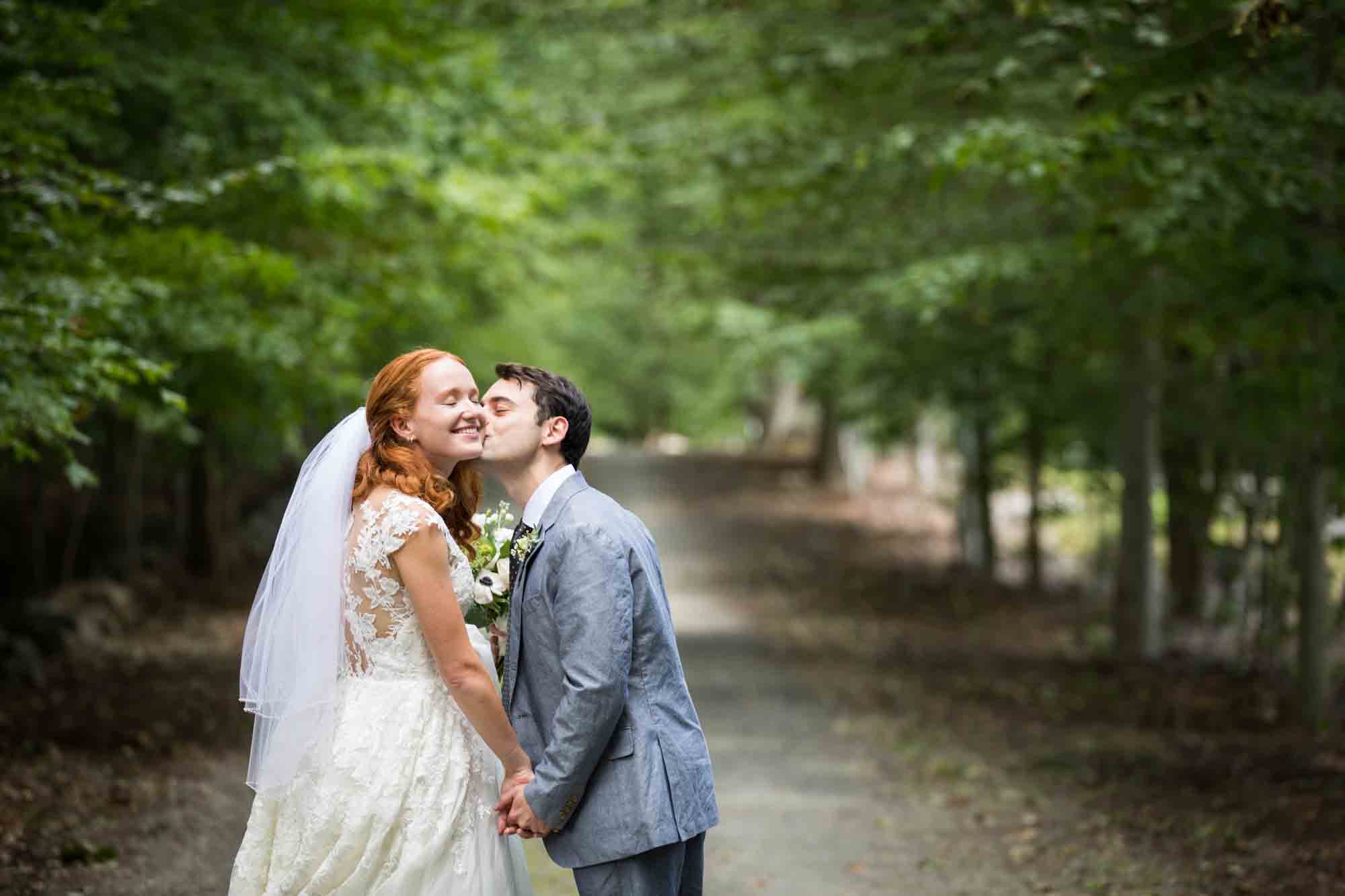 Groom kissing bride on the cheek in driveway for an article on backyard wedding tips