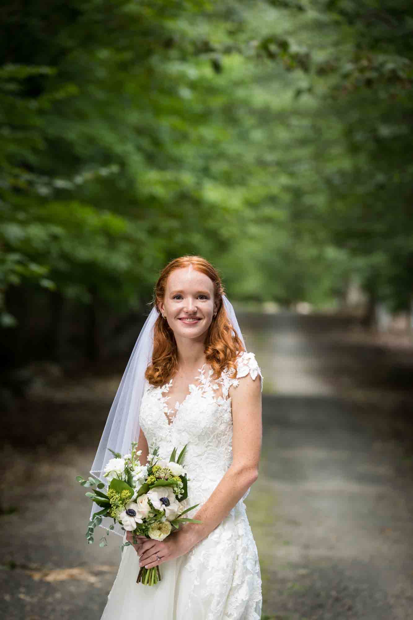 Bride with veil holding flower bouquet on dirt road for an article on backyard wedding tips