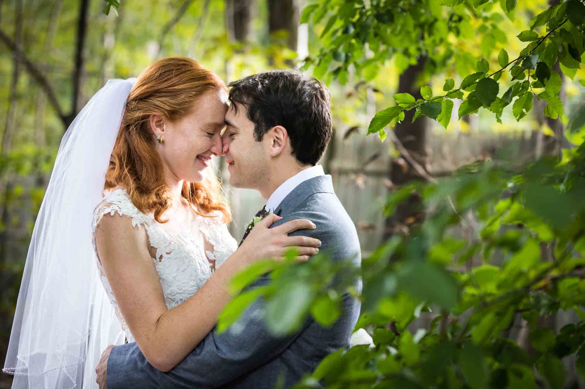 Bride and groom touching foreheads behind trees