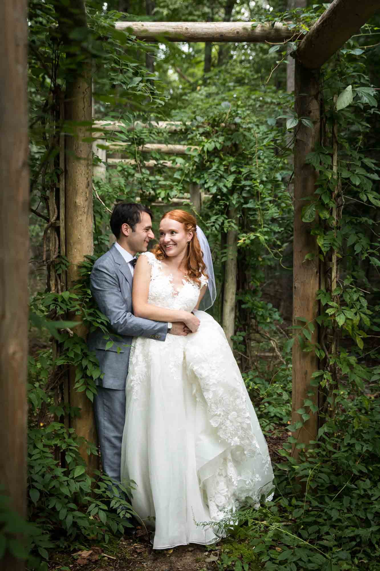 Bride and groom hugging under vine-covered fence