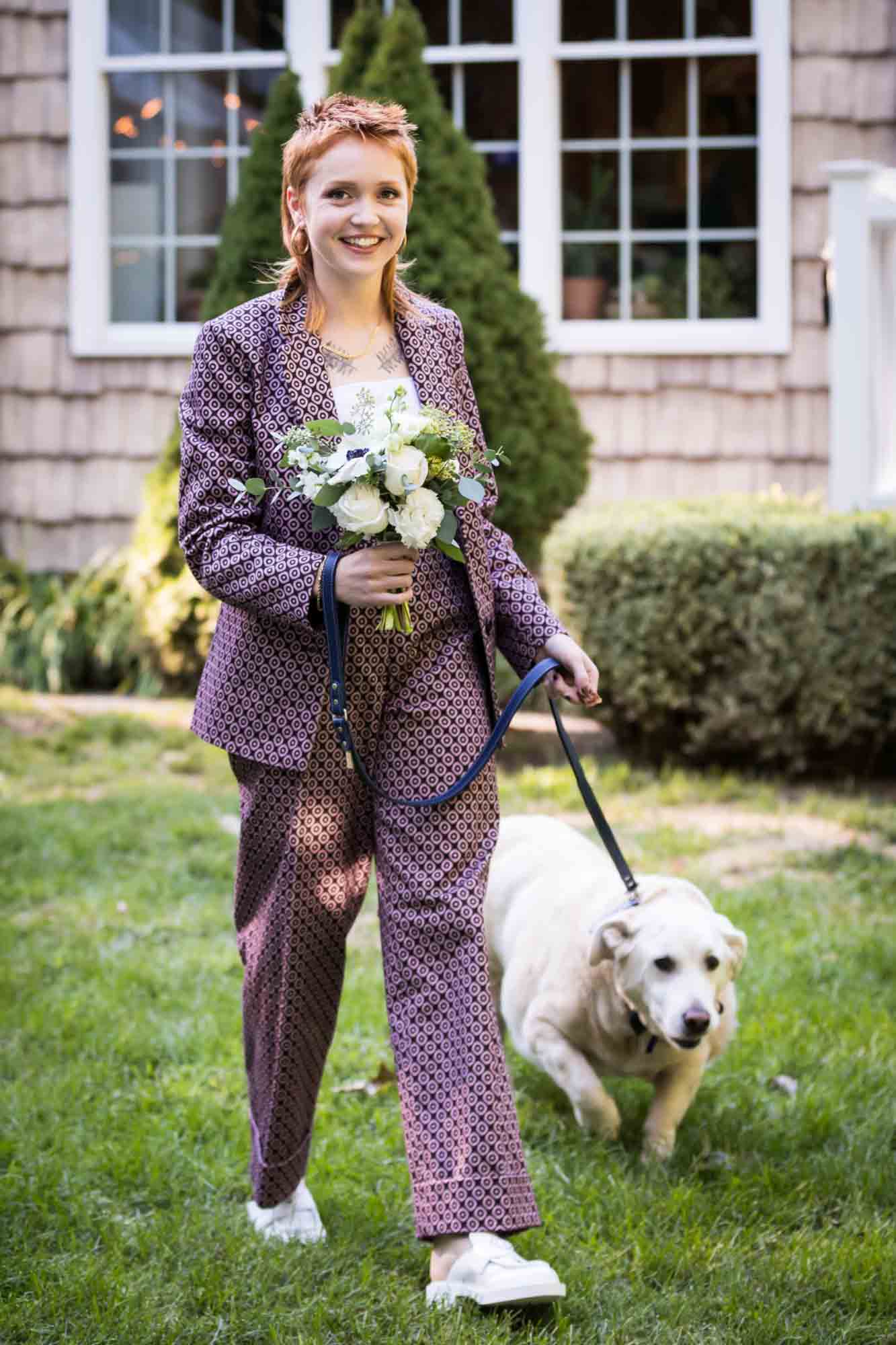 Woman wearing pink suit holding flowers and walking white dog on leash