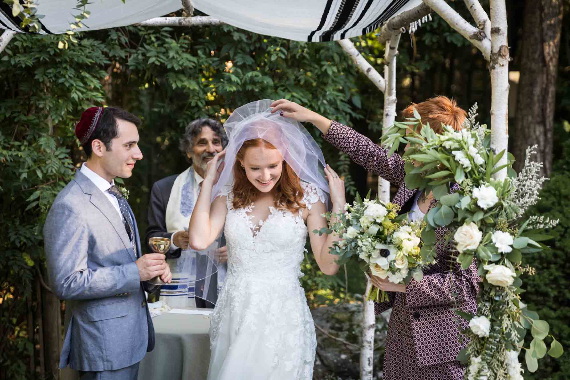 Woman helping bride remove veil during wedding ceremony